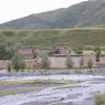 Tibetan earthen houses and prayer flags above a river.