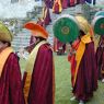 A procession of monks wearing yellow hats and playing clarinets (gyaling) and pole drums.